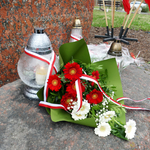 Zdjęcie przedstawia bukiet kwiatów i znicz złożone przy pomniku poległych Katyniaków.