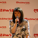 Zdjęcie przedstawia przemawiająca do mikrofonu Ewę Janinę Orzełowską. W tle widoczny jest logotyp Mazowsze serce Polski.